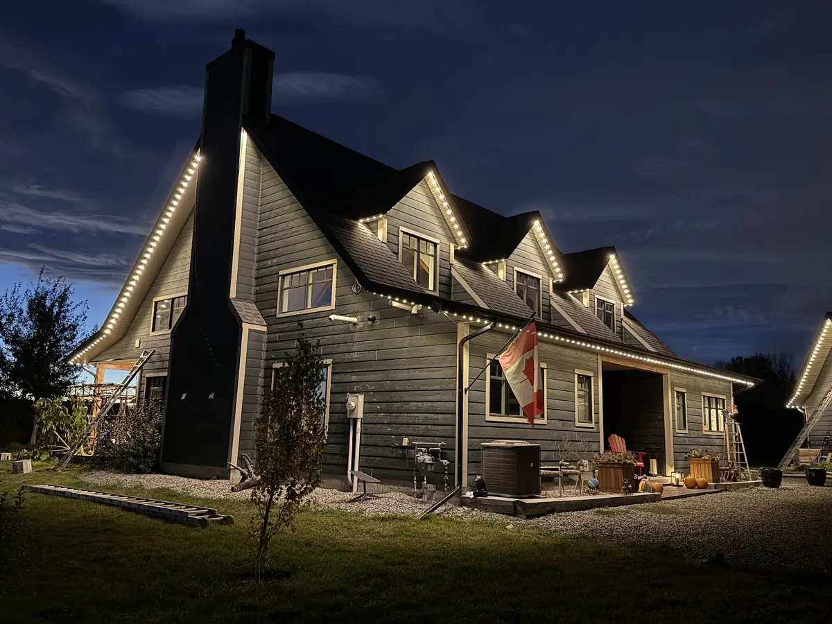 Home with a Canadian flag and warm white permanent lighting at dusk