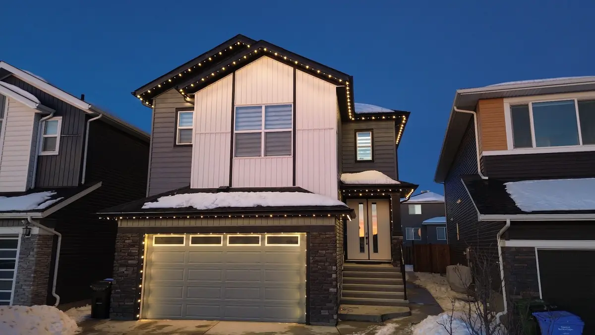 Snowy home with warm white permanent roofline lights at dusk